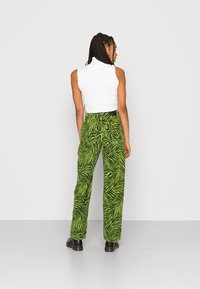 Top sem mangas branco em relevo combinado com calças verdes de cintura alta com padrão de riscas de zebra pretas e sapatos pretos.