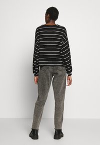 Schwarz-weiß gestreiftes Langarmoberteil mit weitem Ausschnitt, kombiniert mit grauen geraden Hosen. Schwarze Stiefel runden das Outfit ab.