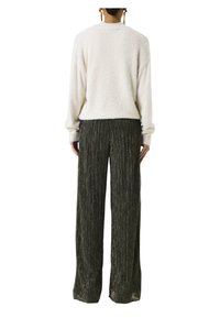 Persoon gekleed in een witte fuzzy trui en zwarte wijde plooibroek met metallic verticale streepjess, gezien vanuit de rug.