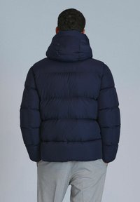 Marinefarbener Puffer-Jacke mit hohem Kragen und gestepptem Design. Mit einer glatten Textur und dicker Polsterung für Wärmeisolierung.