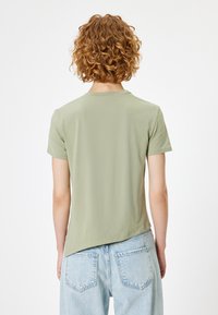 Kortærmet, lys olivengrøn t-shirt med rund hals og buet kant, parret med lyseblå denimjeans i en afslappet pasform.