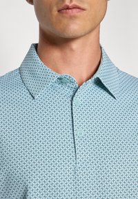 Light blue patterned polo shirt featuring a collared neck and three matching buttons. The fabric has a textured geometric design.