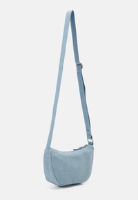 Světle modrá látková crossbody taška s nastavitelným popruhem a zipovým uzávěrem, vystavená na jednobarevném bílém pozadí.