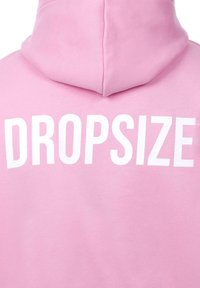 Felpa rosa con una grande stampa bianca del testo "DROPSIZE" sul retro. Il tessuto appare morbido e leggermente strutturato.