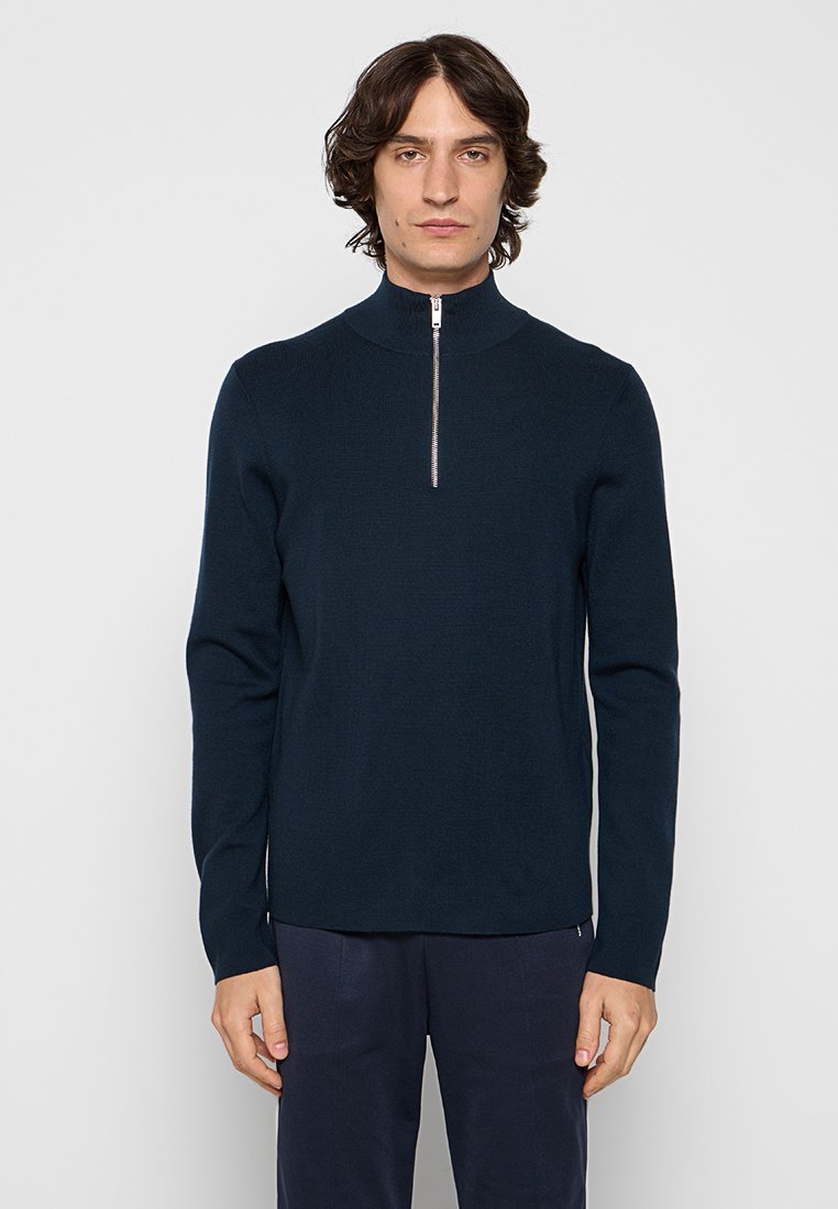 Marinekleurige zip-neck sweater van gebreid materiaal, met een hoge kraag en lange mouwen. Soepele textuur met een minimaal design en subtiele zilveren ritsdetails.