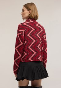 Vícebarevný svetr s červeným, růžovým a černým cikcak vzorem s texturovaným povrchem. Stylizován s černou rozšířenou sukní.