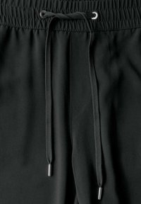 Černé joggingové kalhoty s elastickým pasem, vybavené šňůrkou s metalickými konci a boční kapsou. Hladká textura látky.