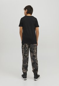 T-shirt nera in cotone abbinata a pantaloni cargo grigi in camouflage con tasche laterali, polsini elasticizzati e sneakers nere alte.