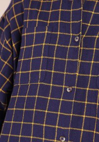 Chemise bleu marine avec un motif à carreaux orange, gros plan montrant la texture du tissu et trois boutons visibles sur le devant.