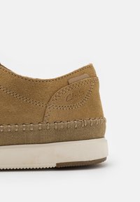 talon de chaussure en daim marron avec bordure en tissu beige cousu et semelle en caoutchouc blanc, logo Clarks embossé sur la tige latérale.