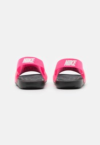 Sandały klapki Nike w jaskrawym różu z czarnymi podeszwami. Posiadają szerokie materiałowe paski oraz wytłoczone detale na pięcie. Lekkie, otwarte z tyłu.