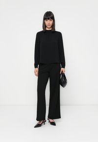 Black long-sleeve top with a textured finish, paired with wide-leg black trousers. Completed with black heels and a soft, gathered handbag.