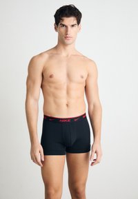 Schwarze Stretch-Boxershorts mit einem roten Nike-Logo am Bund. Das Design ist eng anliegend mit einer glatten Textur und einer Länge bis zur Mitte des Oberschenkels.
