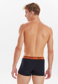 Zwarte boxershorts met een oranje JBS tailleband, snug fit, gladde stof, gezien van de achterkant, waarbij de tailleband en het achterontwerp worden getoond.