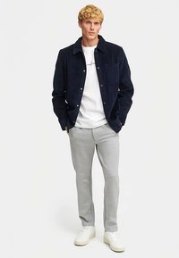 Navy corduroy shirt jacket with a collar and button closure, worn over a white T-shirt, paired with light grey joggers and white sneakers.