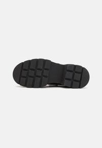 Black rubber shoe sole with a patterned tread. Features square and rectangular indentations for grip, flat profile, and rounded edges.