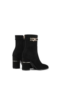 Stivali alla caviglia in suede nero con tacco a blocco. Caratterizzati da un accento in catena dorata e una cerniera laterale. Texture liscia e design elegante.