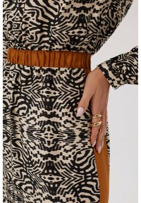 Sukienka w zwierzęcy wzór w czerni i beżu, zebrana w brązowej talii. Teksturowany materiał o gładkim wykończeniu i warstwowych akcentach po bokach.