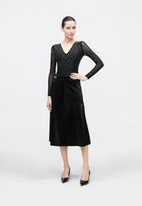 Μαύρο ολόσωμο κορμάκι με μακριά μανίκια και V-λαιμόκοψη διακοσμημένη με ασημένιους τρουκς, σε συνδυασμό με μαύρη δερμάτινη φούστα έως το γόνατο.