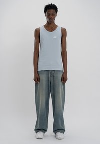 Top de malha canelada azul claro com um logótipo branco no peito, combinado com jeans baggy desbotados e ténis brancos.