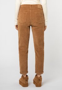 Braune Cord-Hosen mit geradem Schnitt, ausgestattet mit umgeschlagenen Säumen und Gesäßtaschen. Tragen mit tanfarbenen Wildleder-Stiefeletten.