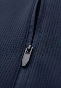 Marinblå mönstrad tyg med en närbild av en svart dragkedja som har en "ombre"-logotyp, vilket framhäver textur och design detaljer.