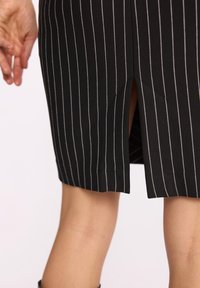 Czarna spódnica z pionowymi białymi paskami, z centralnym rozcięciem na dole. Materiał wydaje się gładki z wyraźną strukturą.