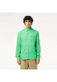 Camicia verde a maniche lunghe in tessuto leggero, con taschino sul petto e un piccolo logo sul lato sinistro.
