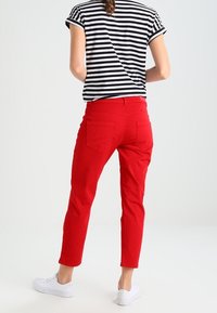 Červené bavlněné kalhoty se zúženými nohavicemi a zadními kapsami, zkombinované s černo-bílým pruhovaným tričkem s krátkým rukávem a bílými teniskami.