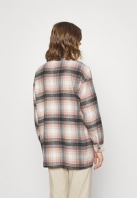 Button-up flannel shirt in pink, black, and white plaid pattern. Features a relaxed fit, long sleeves, and two-button cuff detail.