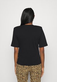 Svart t-shirt med korta ärmar, rund halsringning och slät bomullstextur, ihop med mönstrade leopardmönstrade byxor. Bakifrån.