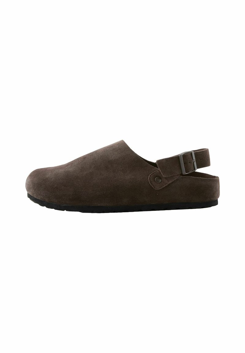 Braune Wildlederschlüpfschuhe mit niedrigem Absatz, verstellbarem Metallverschluss und strukturierten Gummisohlen, ausgestattet mit einer glatten, abgerundeten Zehenpartie und einem schlichten Design.