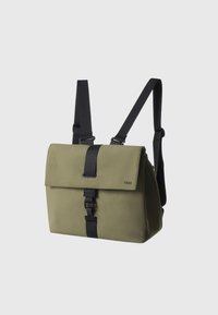 Olive green backpack with a flap closure, black straps, and a buckle. Smooth texture and minimalistic design, featuring branding on the front.