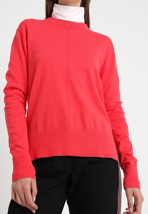Pull en corail à manches longues, coupe droite, ourlet côtelé et col rond, superposé à un col roulé blanc.