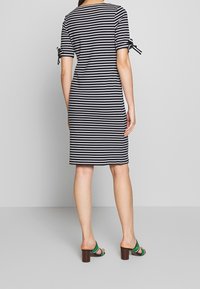 Vestido a rayas en blanco y negro con mangas cortas, con lazos decorativos en las mangas. Combinado con sandalias de tacón cuadrado marrones.