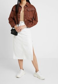 Ruskea cropped-denim-takki etutaskuilla, valkoinen denim-midi-hame sivuaukolla ja valkoiset lenkkarit. Pieni musta olkalaukku.