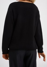 Czarny sweter dzianinowy z szerokim, prążkowanym dekoltem i teksturowanym tyłem górnej części. Długie rękawy i luźny krój. Widoczne prążkowanie w całej strukturze.