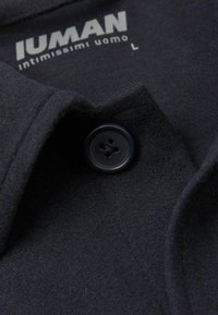 Camisa de mezcla de lana negra con cuello con solapa y cierre frontal de botones. La tela tiene un acabado suave y texturizado.