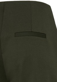 Gros plan sur un tissu vert foncé avec une poche passepoilée horizontale, montrant la texture et les détails des coutures.