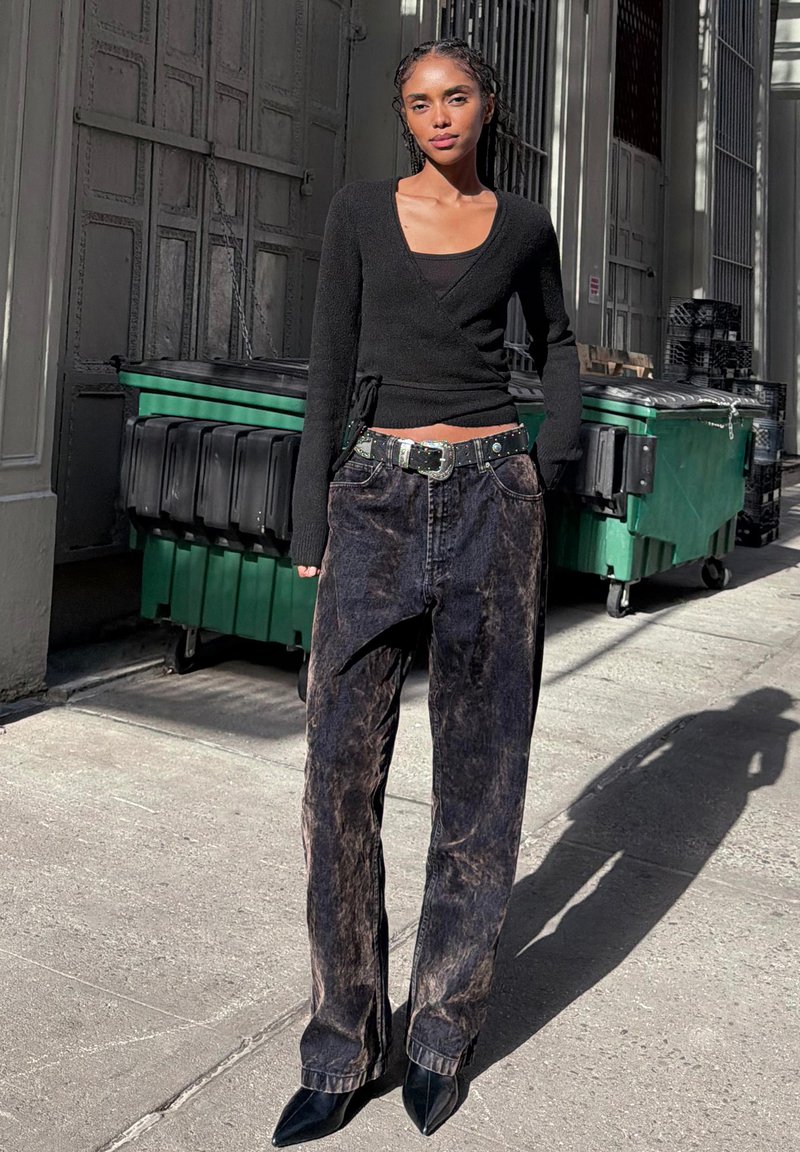 Černý svetr s dlouhými rukávy, kombinovaný s tmavými, vybledlými džínami. Úzký kožený pásek se stříbrnou sponou. Špičaté černé boty.