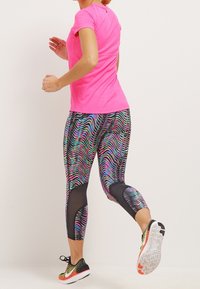 T-shirt de sport rose associé à des leggings noirs à motifs colorés ; tissu texturé, design ajusté, chaussures de course avec une semelle multicolore.