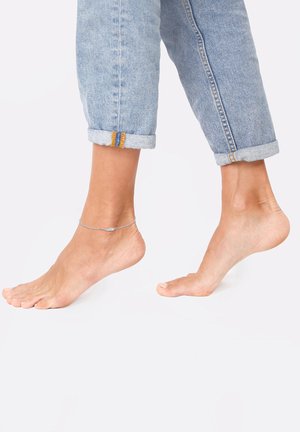 Anklet made of thin silver chain, worn on an ankle, with a simple design. Light blue denim jeans are rolled at the cuffs.