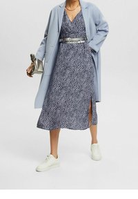 Světle modrý kabát přes námořnické šaty s bílými abstraktními vzory, s bočním rozparkem, stříbrným páskem a bílými teniskami. Součástí je také stříbrná kabelka.