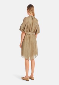 Khakifarbenes Leinenkleid mit Puffärmeln, tailliertem Bund und knielangem Saum. Glatte Textur, dezenter Glanz und durchscheinender Stoff am unteren Ende.