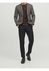Grau-brauner Blazer über einem dunkelbraunen Hemd, kombiniert mit schwarzen Hosen und glänzenden schwarzen Schuhen. Maßgeschneiderte Passform, lässiger Stil.