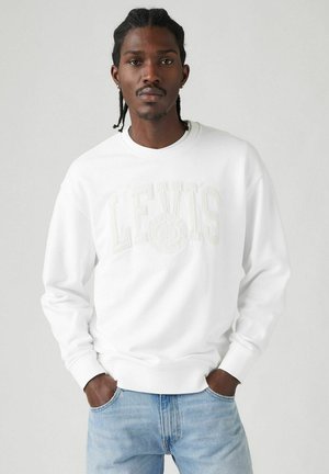 Sudadera blanca con el logotipo en relieve "LEVI'S" en el pecho, puños acanalados y un corte relajado, combinada con jeans de color azul claro.