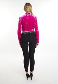 Feszes fekete leggings és egy rózsaszín bársony felső, magas gallérral, amely deréknál gyöngyökkel díszített, és hátul kulcslyuk nyílással rendelkezik.