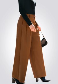 Bruine wijde broek met een gladde textuur, hoge taille, plooien aan de voorkant en gecombineerd met zwarte stilettos en een kleine zwarte handtas.
