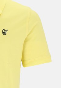 Polo giallo a maniche corte, realizzato in tessuto testurizzato, con un piccolo logo ricamato nero sul petto.
