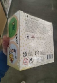 Rechteckiger Karton mit einem gelben Pünktchenmuster. Enthält bunte Illustrationen, Sicherheitsetiketten und Text auf einem hellen Hintergrund.